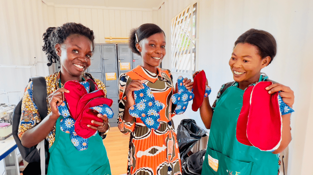 Omba Noela, Kisera Esther and Rebecca Kanjiliji proudly display the reusable sanitary pads they made, showcasing their new sewing skills and commitment to supporting women in the refugee camp with affordable menstrual products. 